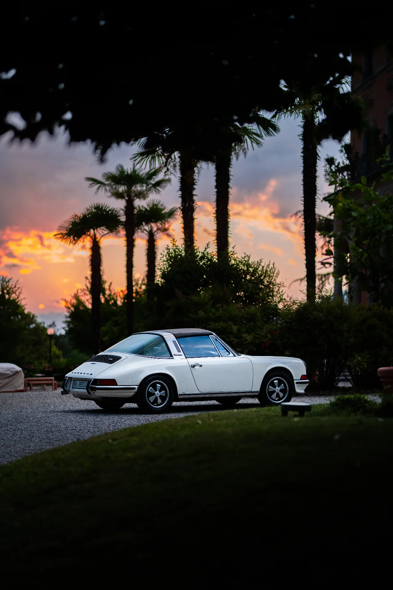 Porsche bianca al tramonto tra le palme davanti alla villa